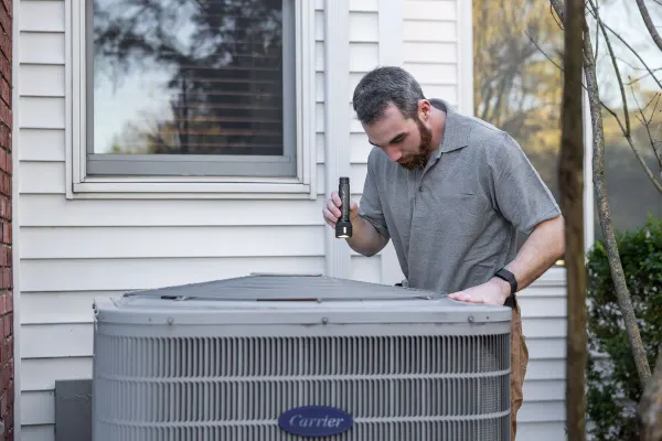 A technician inspecting a residential outdoor AC condenser with a flashlight